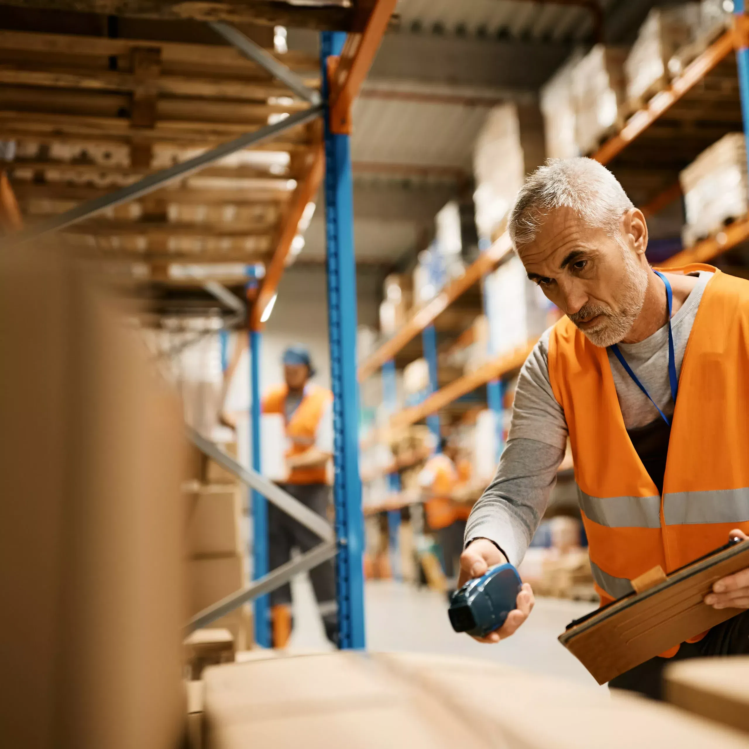 Mature warehouse worker using touchpad and scanning cardboard boxes at storage compartment.